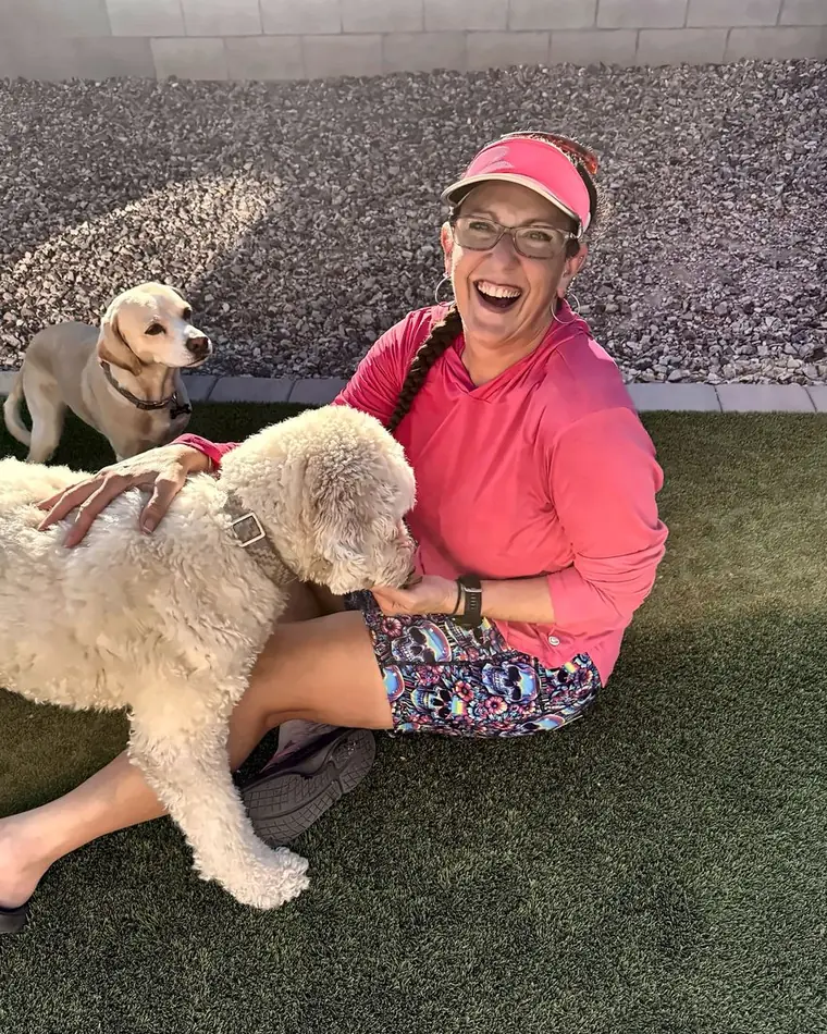 Britni, owner of Poopsie Daisy, laughing on the turf with a goldendoodle and a yellow lab