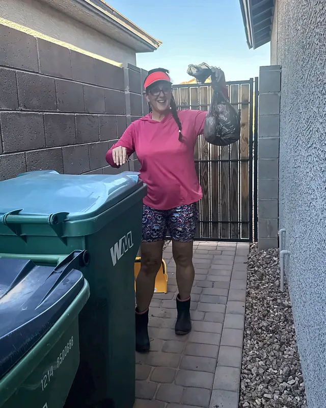 Britni holding up a tied bag next to the trash bins