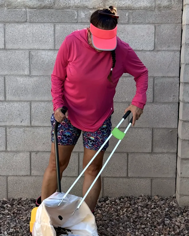 Britni scooping dog waste from desert rock with a long-handled scooper